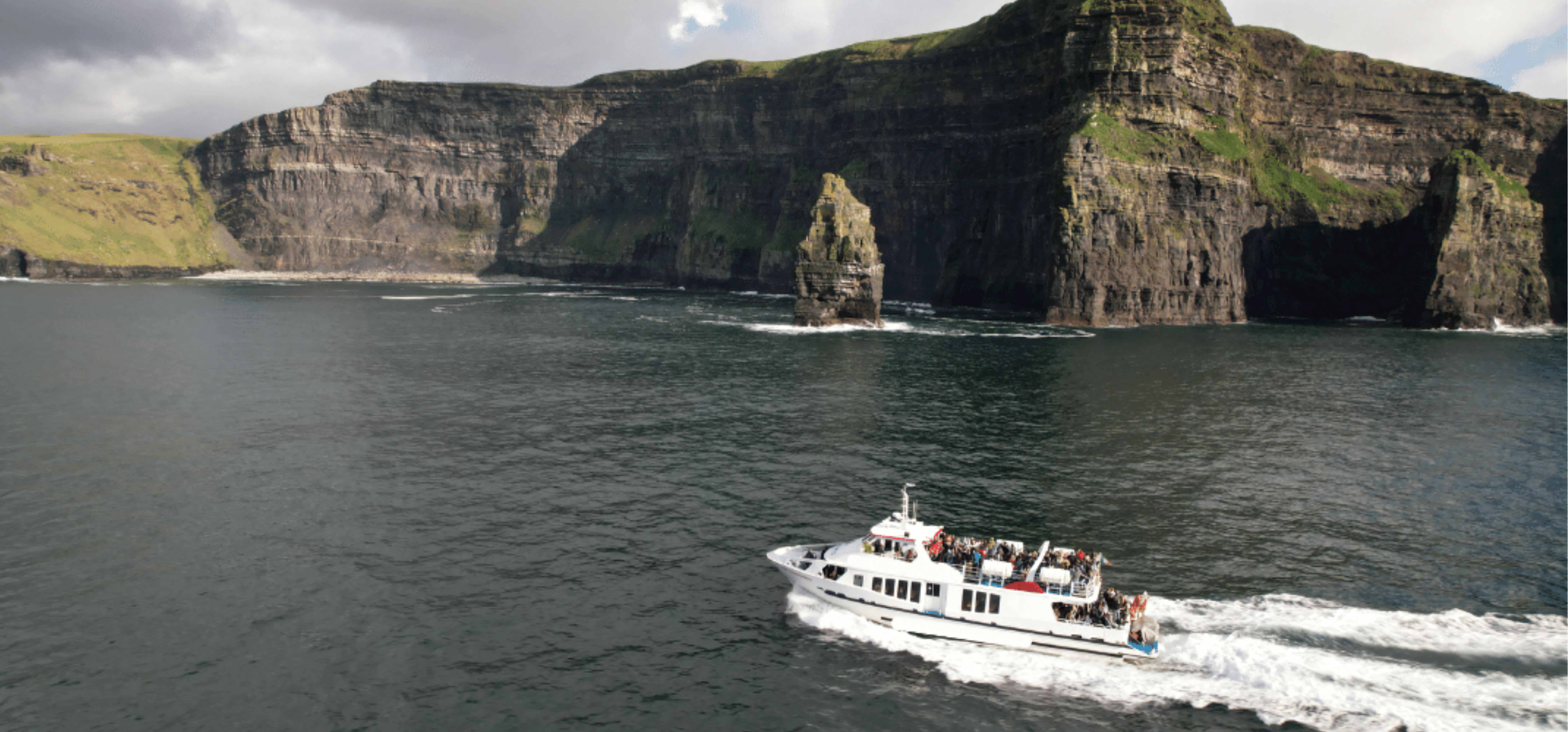 Aerial view of a boat approaching the Cliffs of Moher, Ireland, showcasing rugged coastline and vast ocean.