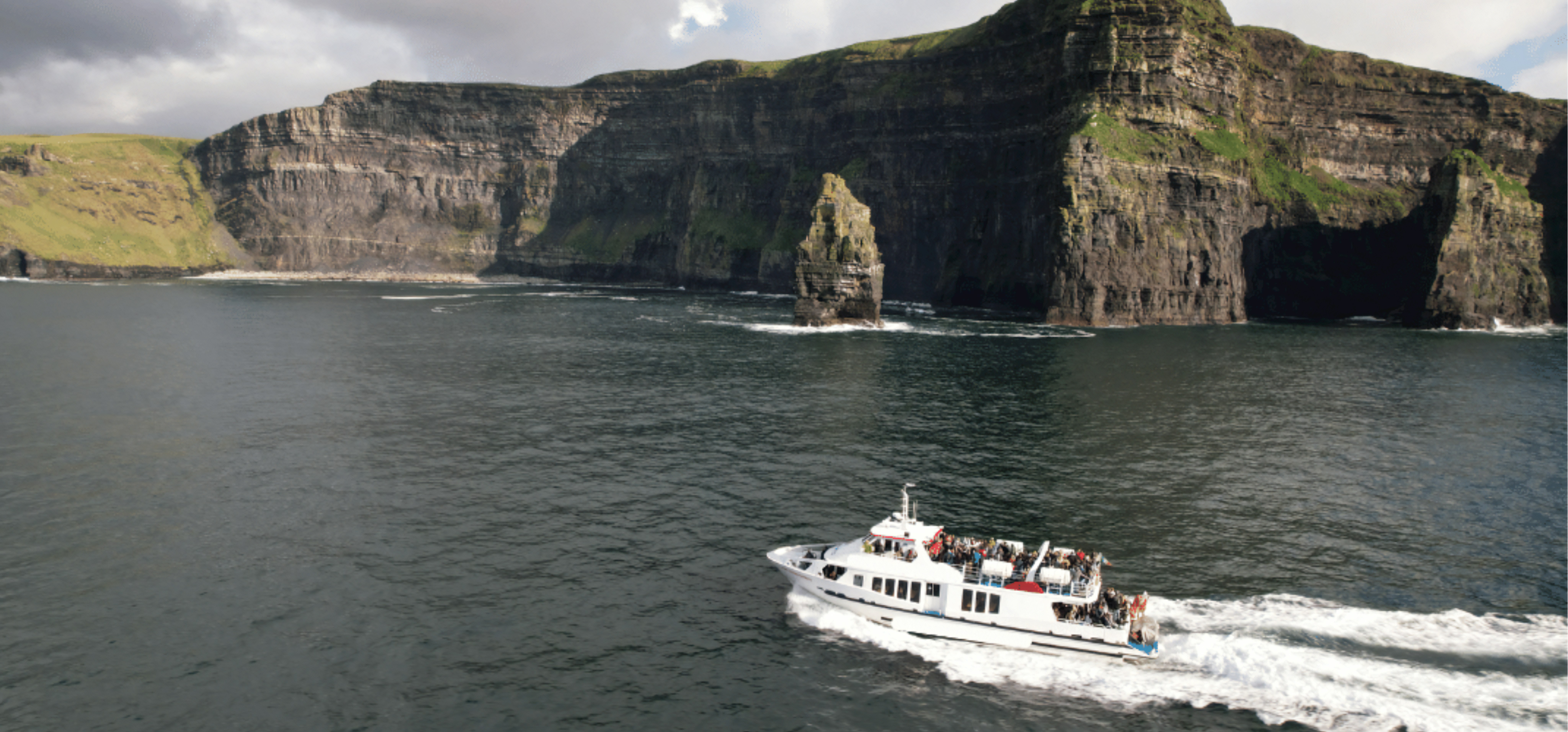 Aerial view of a boat approaching the Cliffs of Moher, Ireland, showcasing rugged coastline and vast ocean.