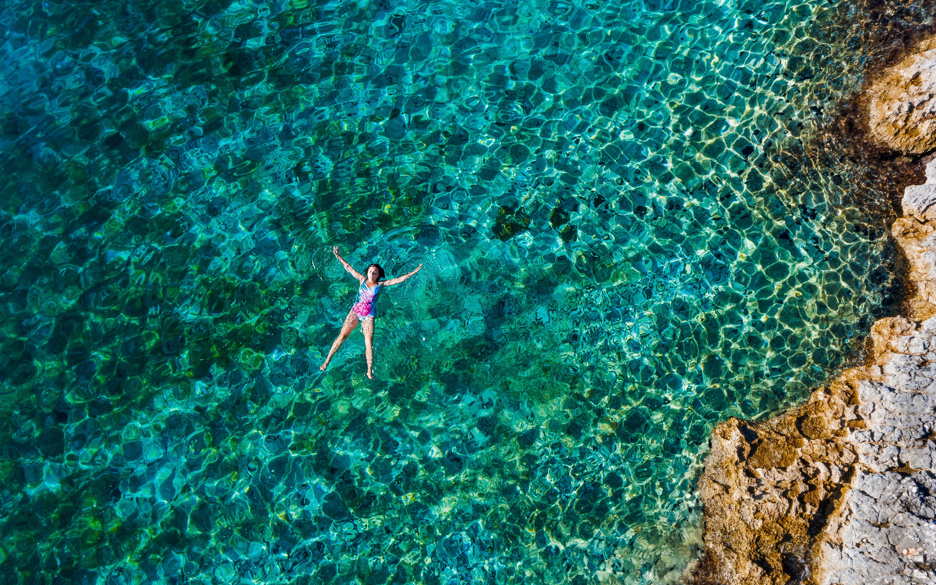 Woman swimming in clear blue lagoon near rocky shore.