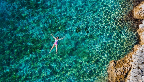 Woman swimming in clear blue lagoon near rocky shore.