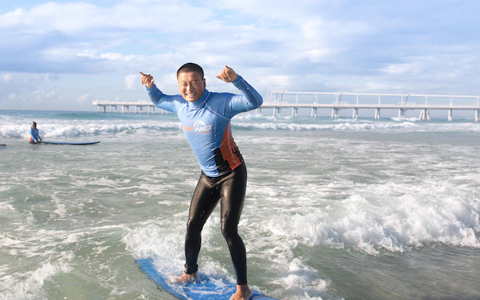 Beginner surfer standing on a board in the ocean near a pier.