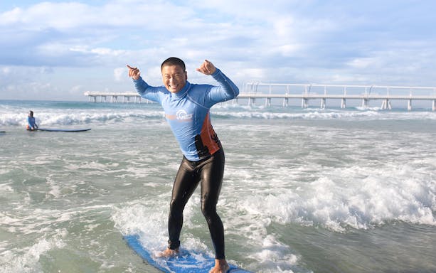 Beginner surfer standing on a board in the ocean near a pier.