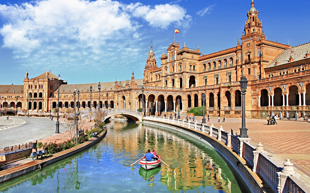 Rowboat on canal at Plaza de España, Seville, with historic building in background.