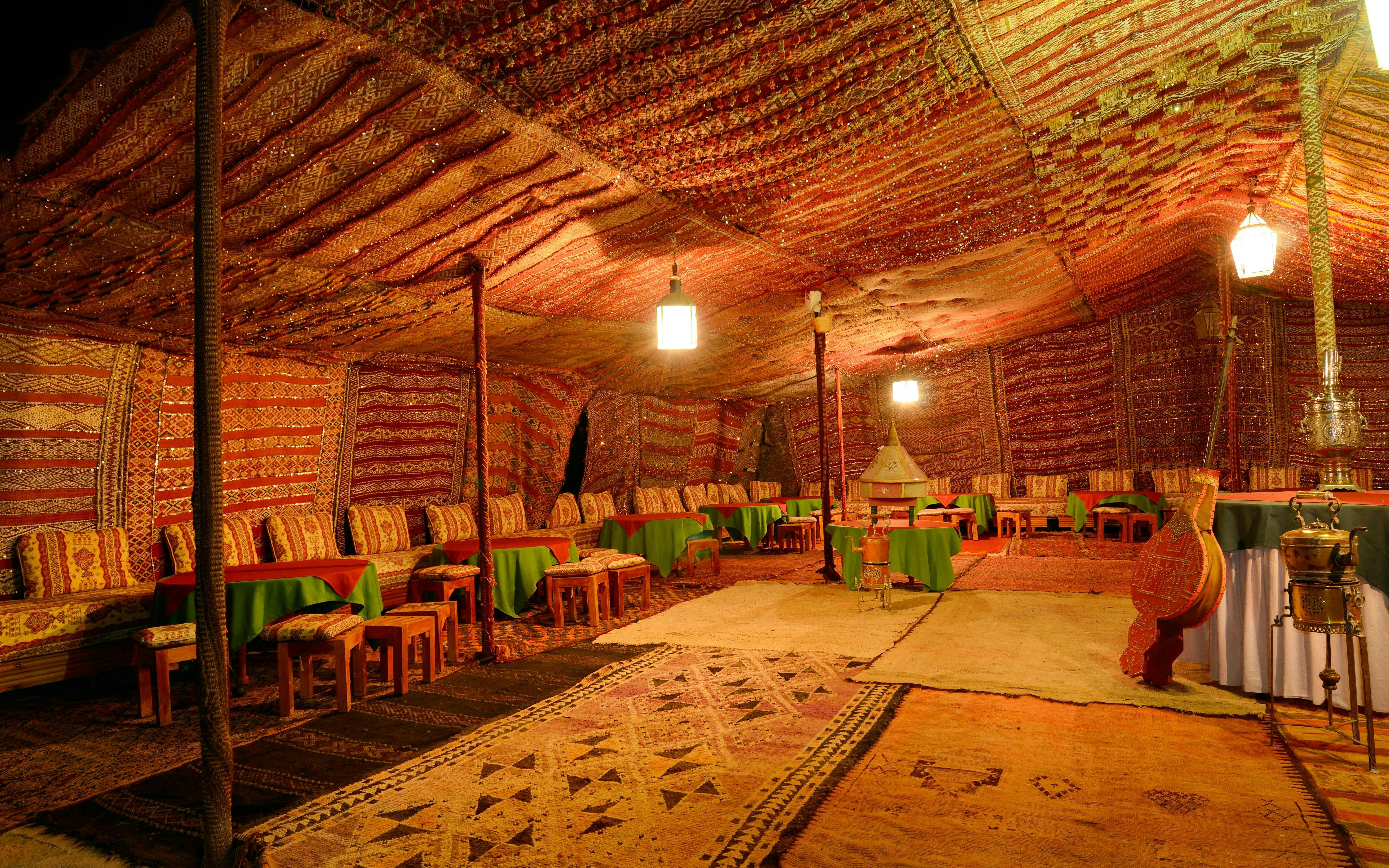 Large Berber tent interior with carpets and seating in Tinerhir, Morocco at night.