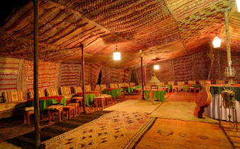 Large Berber tent interior with carpets and seating in Tinerhir, Morocco at night.