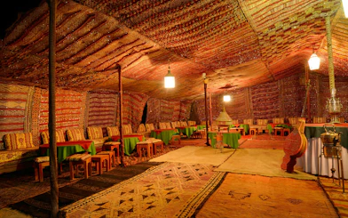 Large Berber tent interior with carpets and seating in Tinerhir, Morocco at night.