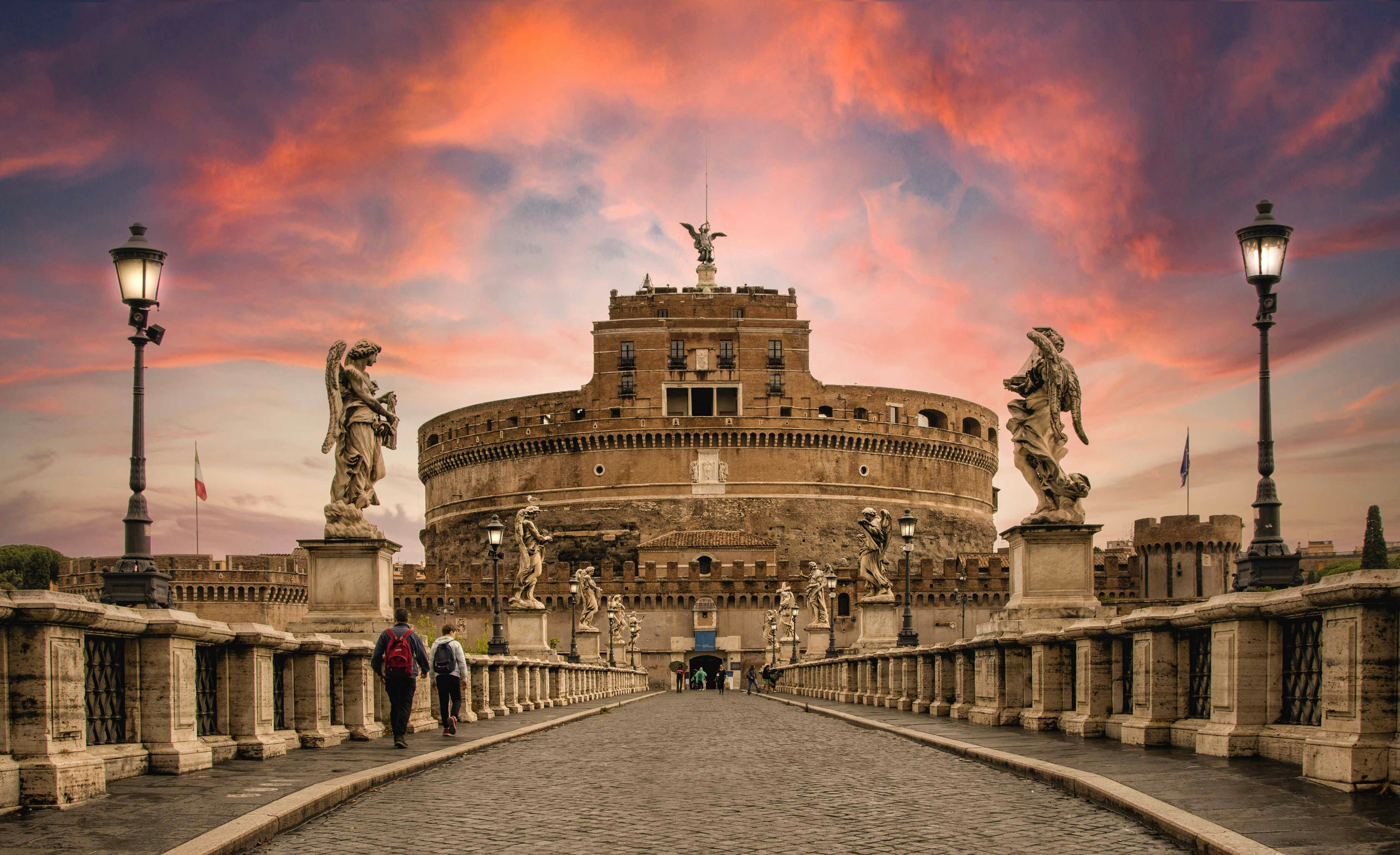 Castel Sant'Angelo in Rome at sunset, viewed from the bridge with statues and lamps.