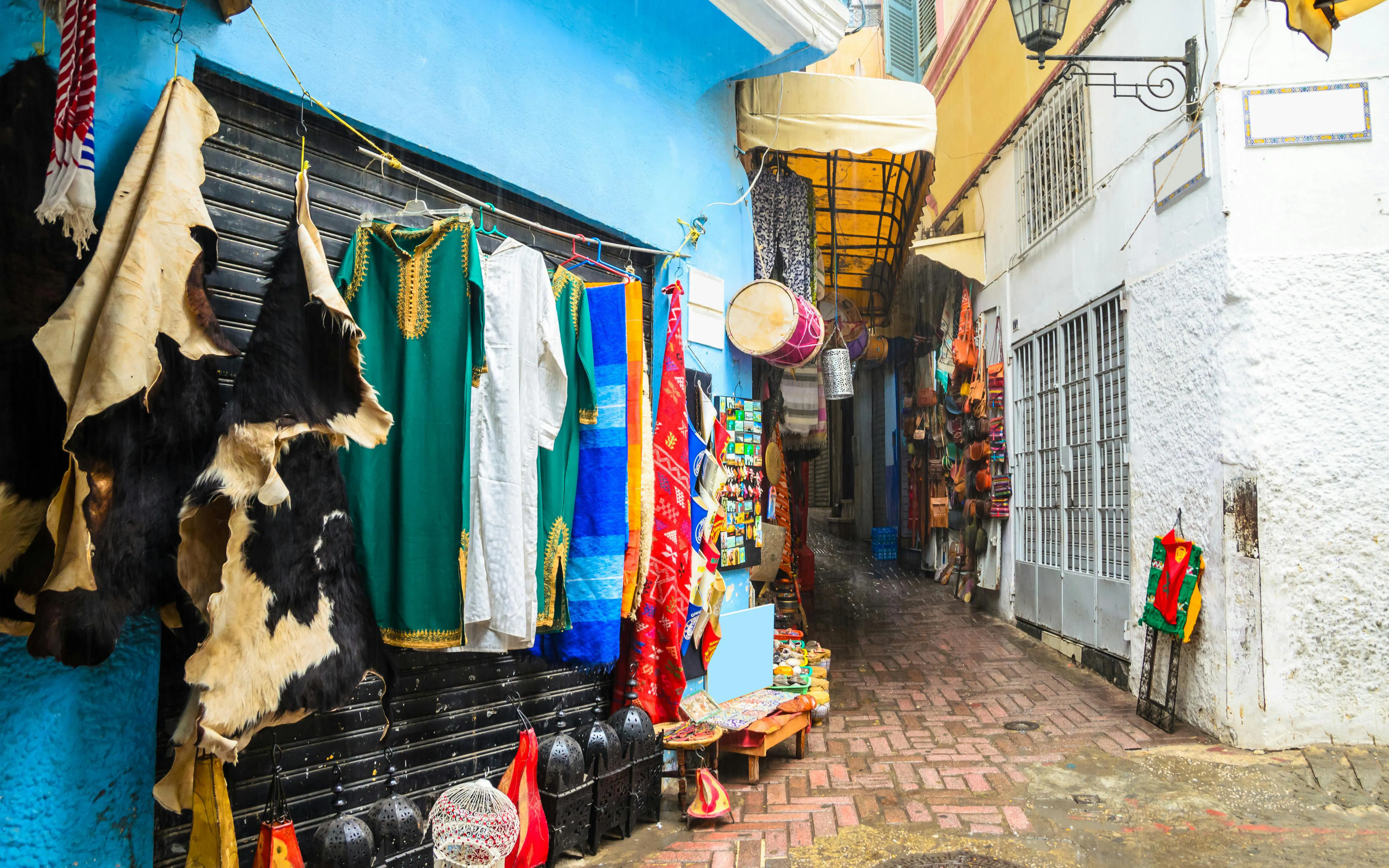 Street market in the medina of Tangier with colorful garments and leather goods displayed.