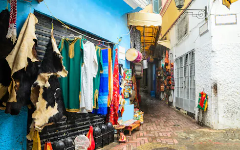 Street market in the medina of Tangier with colorful garments and leather goods displayed.
