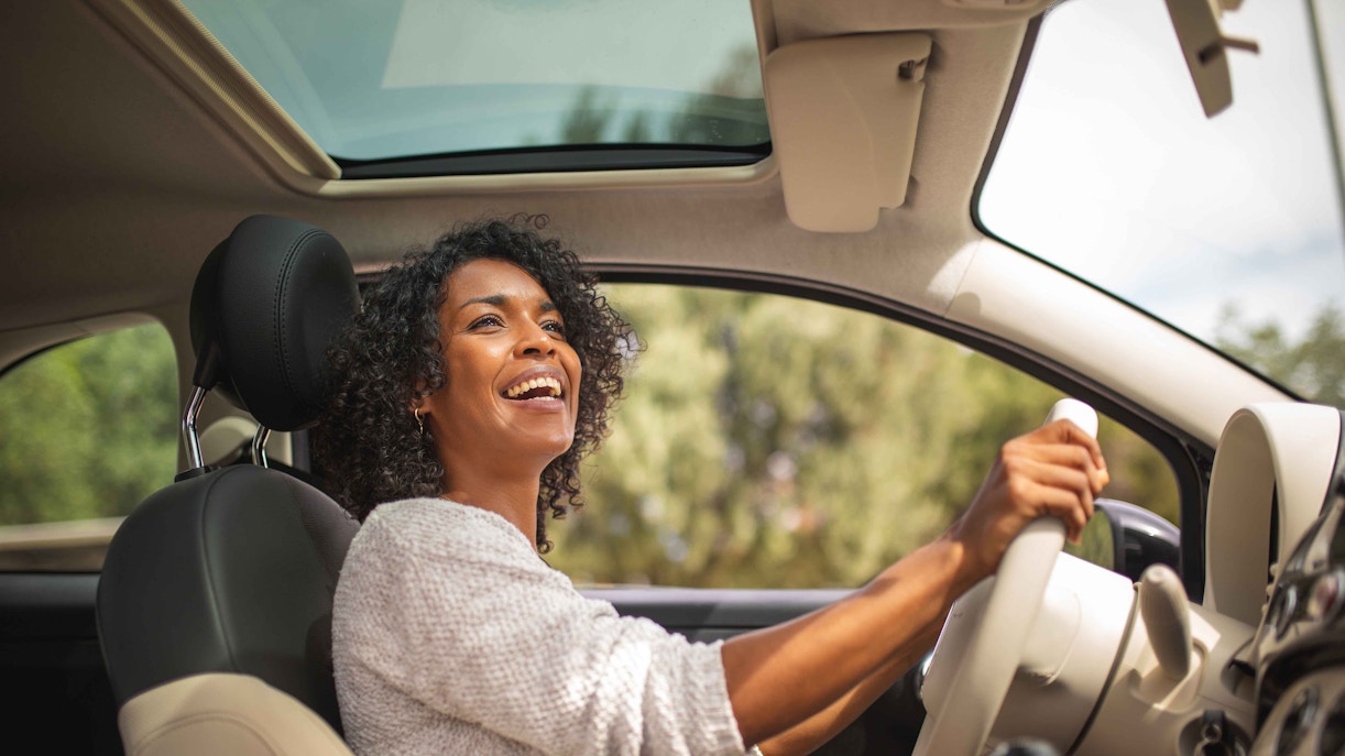 Woman driving a car with a sunroof open, enjoying a scenic view.