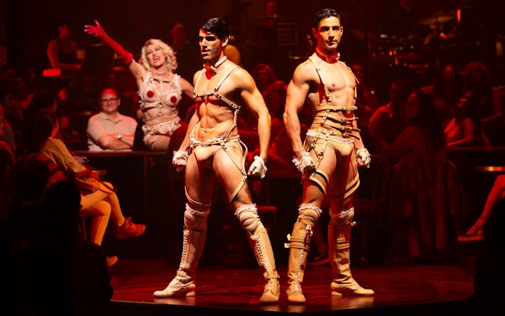 Cabaret performers on stage during a Madrid show, with audience in the background.