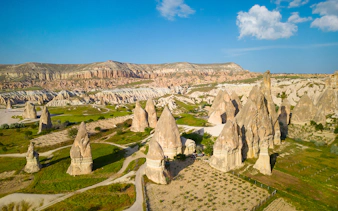 Cappadocia's fairy chimneys at sunrise, Turkey, with green fields and rock formations.