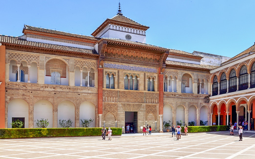 Alcázar of Seville courtyard with intricate arches and visitors exploring.