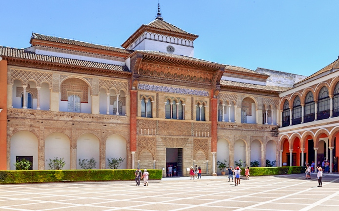 Alcázar of Seville courtyard with intricate arches and visitors exploring.