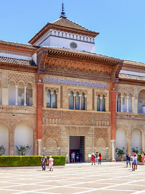 Alcázar of Seville courtyard with intricate arches and visitors exploring.