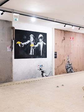 Street art exhibit at The World of Banksy Lisbon featuring iconic mural with figures holding bananas.