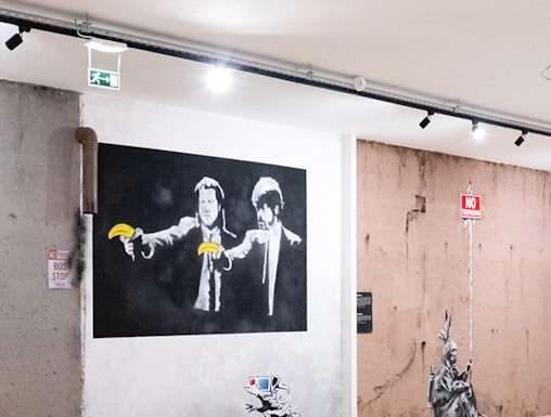 Street art exhibit at The World of Banksy Lisbon featuring iconic mural with figures holding bananas.