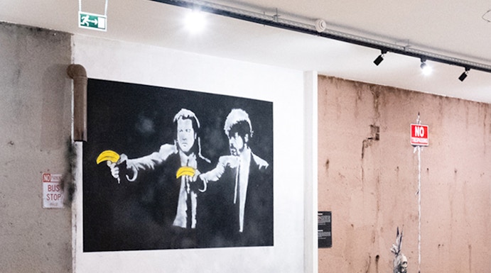 Street art exhibit at The World of Banksy Lisbon featuring iconic mural with figures holding bananas.