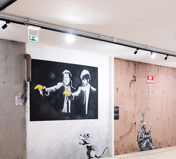 Street art exhibit at The World of Banksy Lisbon featuring iconic mural with figures holding bananas.