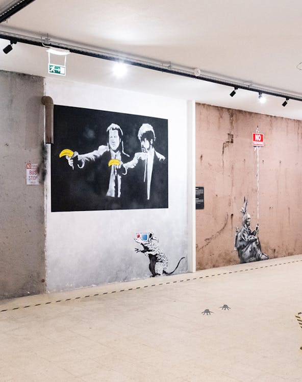 Street art exhibit at The World of Banksy Lisbon featuring iconic mural with figures holding bananas.