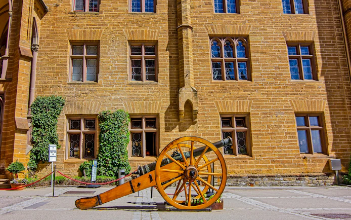 Restored cannon in Hohenzollern Castle courtyard with Gothic architecture, Germany.