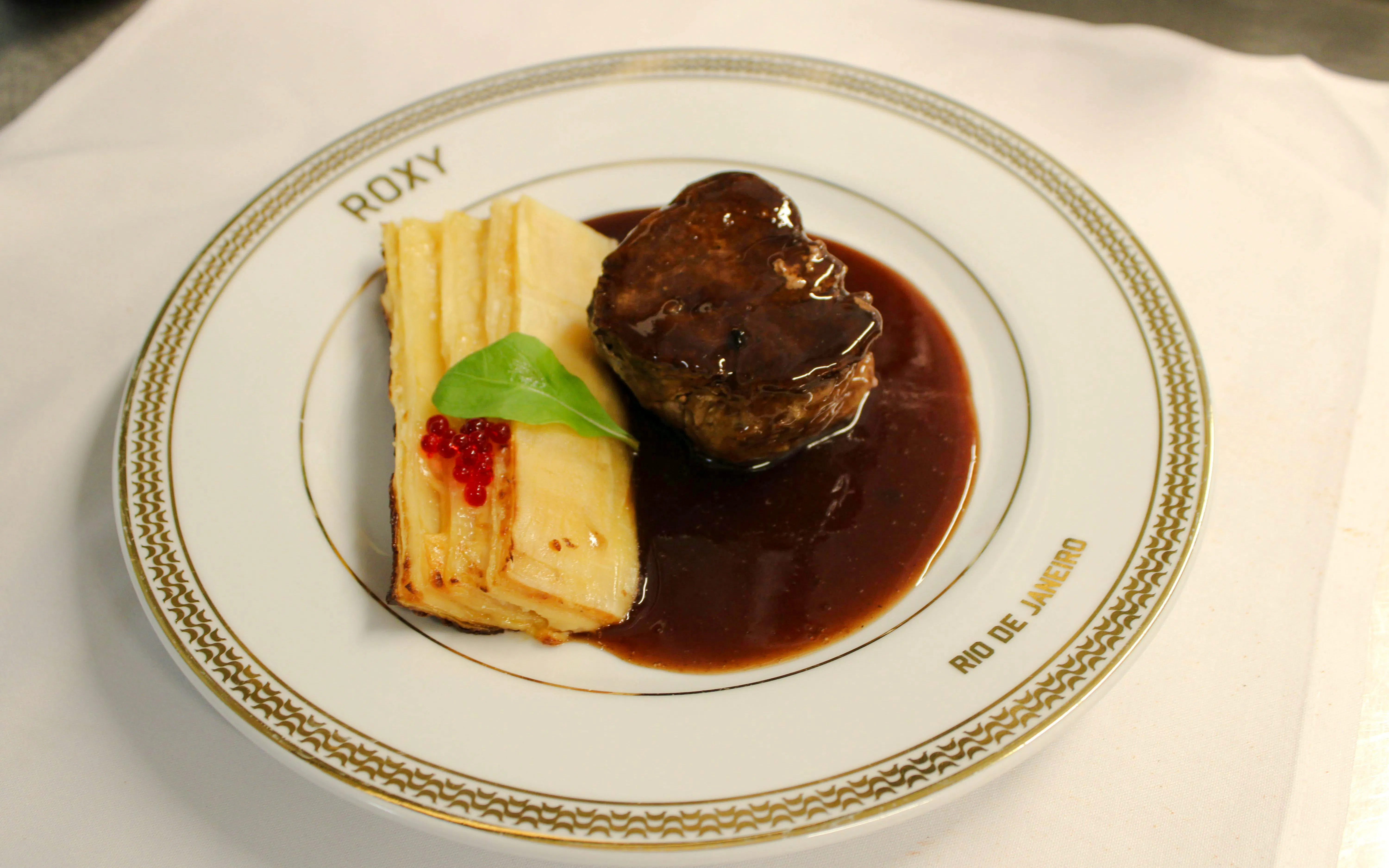 Steak with sauce and layered potatoes on a Roxy plate, Rio de Janeiro dinner show.