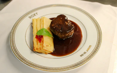 Steak with sauce and layered potatoes on a Roxy plate, Rio de Janeiro dinner show.