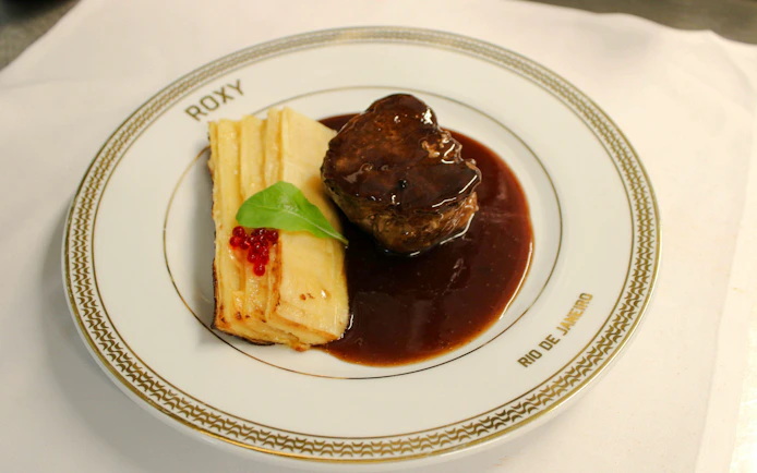 Steak with sauce and layered potatoes on a Roxy plate, Rio de Janeiro dinner show.