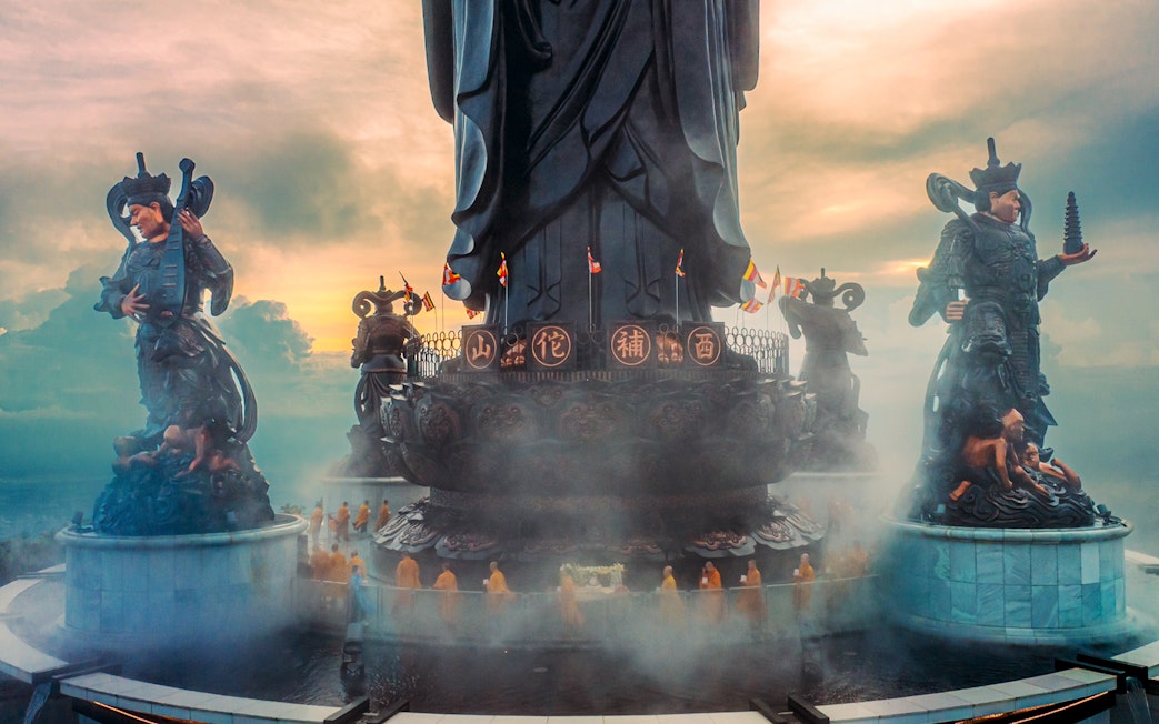 Statues and monks at Hang Pagoda on Ba Den Mountain, Vietnam, during sunrise.