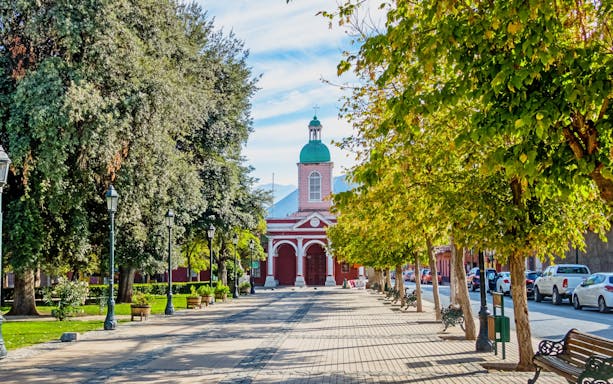 Church in Cajón del Maipo, Chile, with tree-lined path and benches.