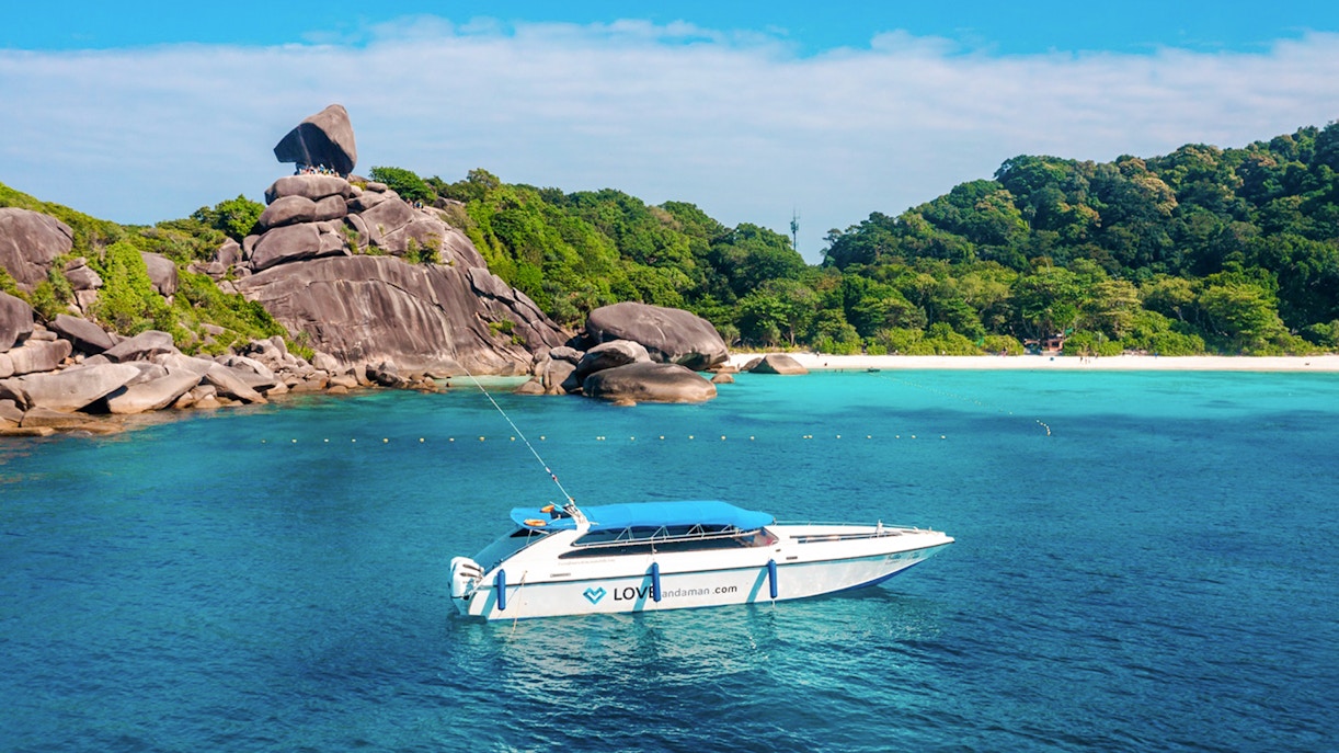 Speed boat approaching Similan Island with rocky shoreline and lush greenery.