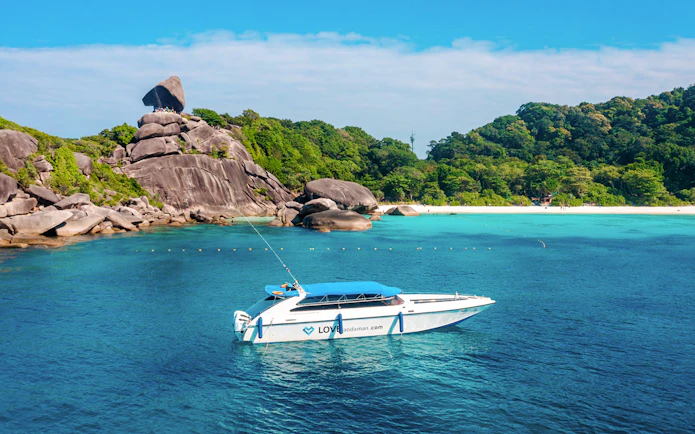 Speed boat approaching Similan Island with rocky shoreline and lush greenery.