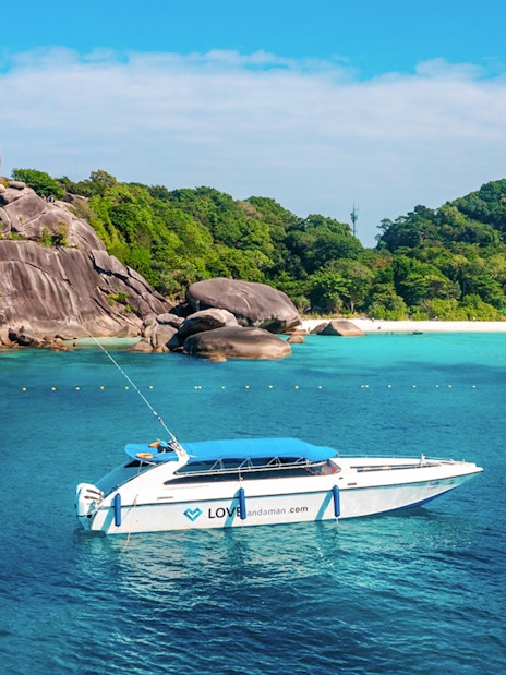 Speed boat approaching Similan Island with rocky shoreline and lush greenery.