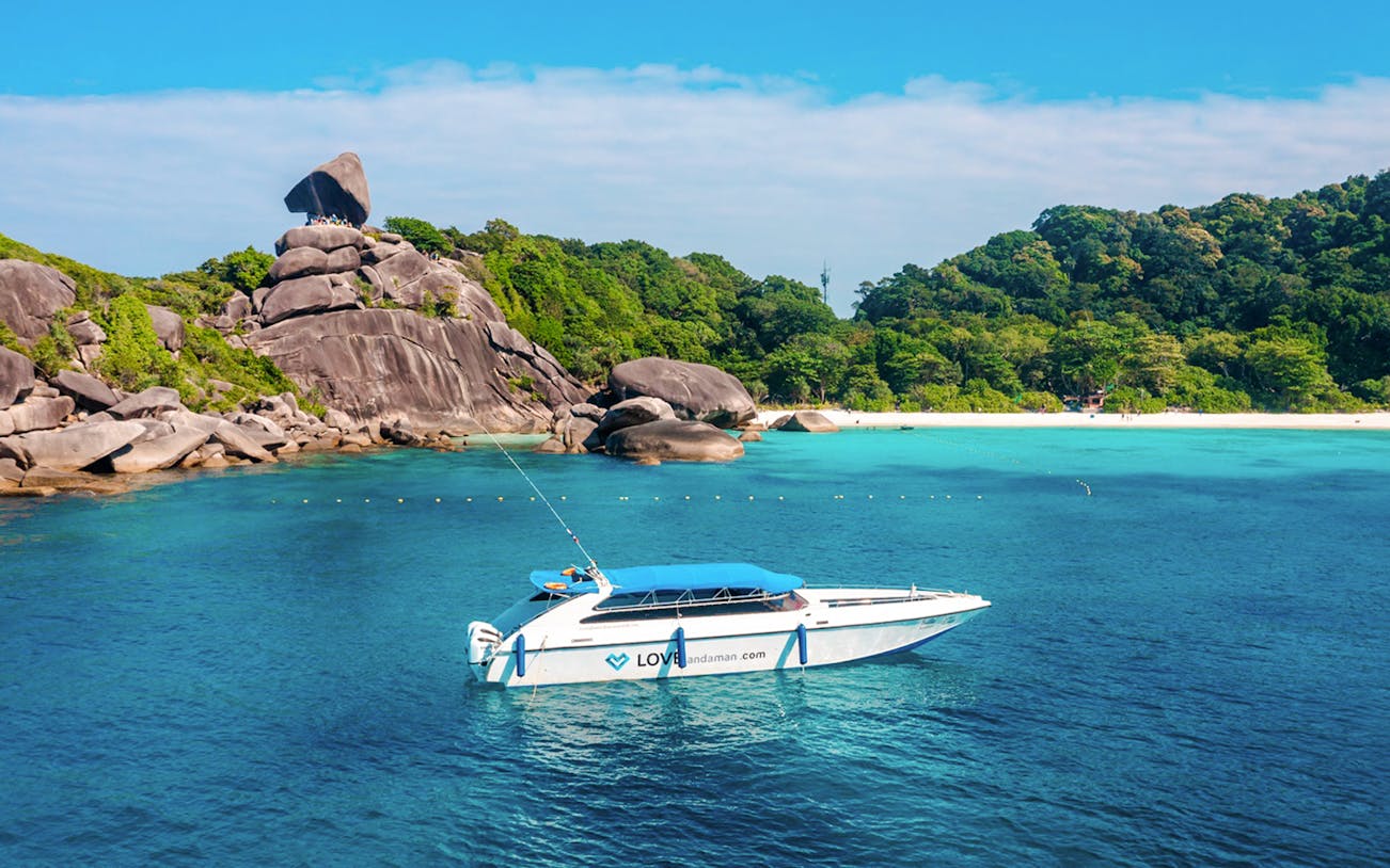 Speed boat approaching Similan Island with rocky shoreline and lush greenery.