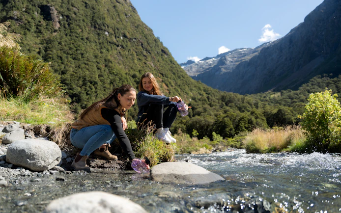 People enjoying a stream in Milford Sound, surrounded by lush mountains.
