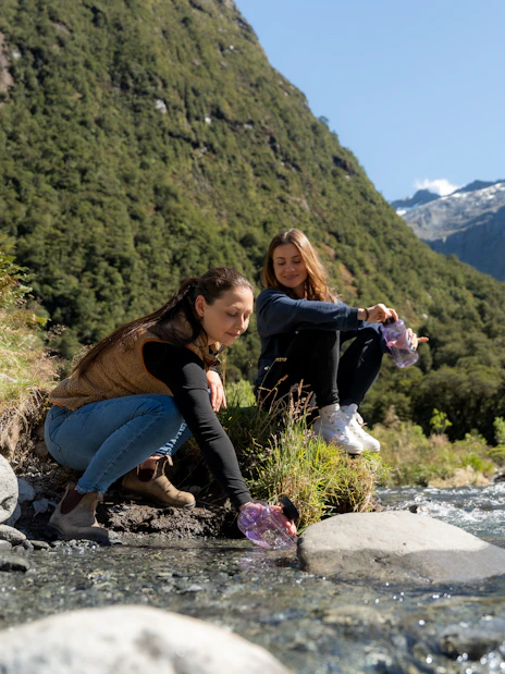 People enjoying a stream in Milford Sound, surrounded by lush mountains.