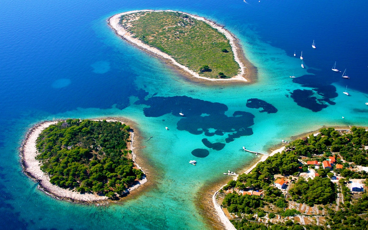 Aerial view of Duga Bay with small islands and sailboats in clear blue water.