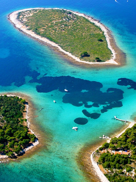 Aerial view of Duga Bay with small islands and sailboats in clear blue water.