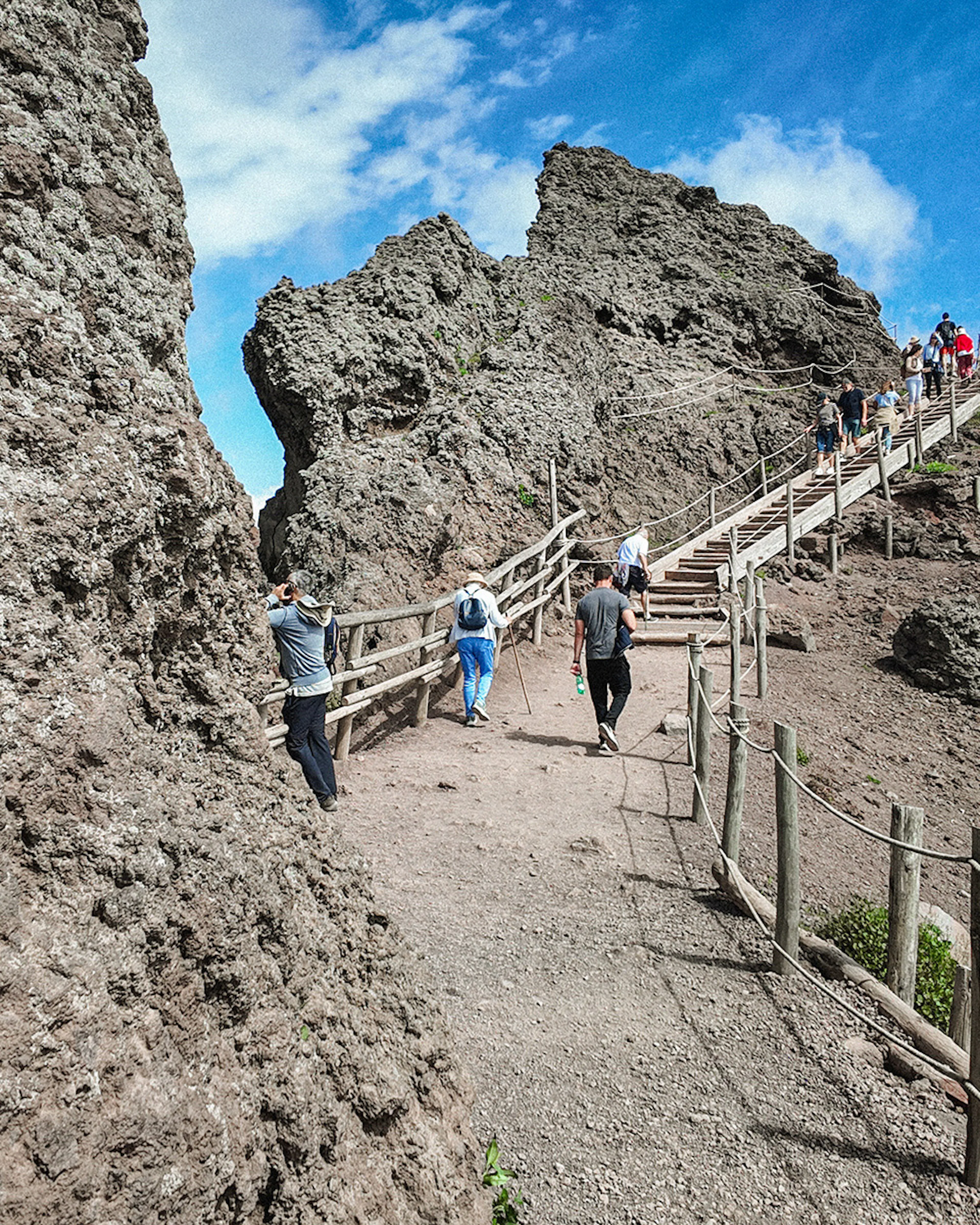 Visitors hiking up the rocky path of Mount Vesuvius under a clear sky.