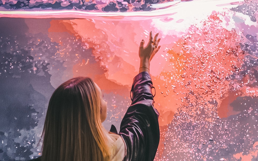 Person reaching towards vibrant abstract art at The Wine Experience.