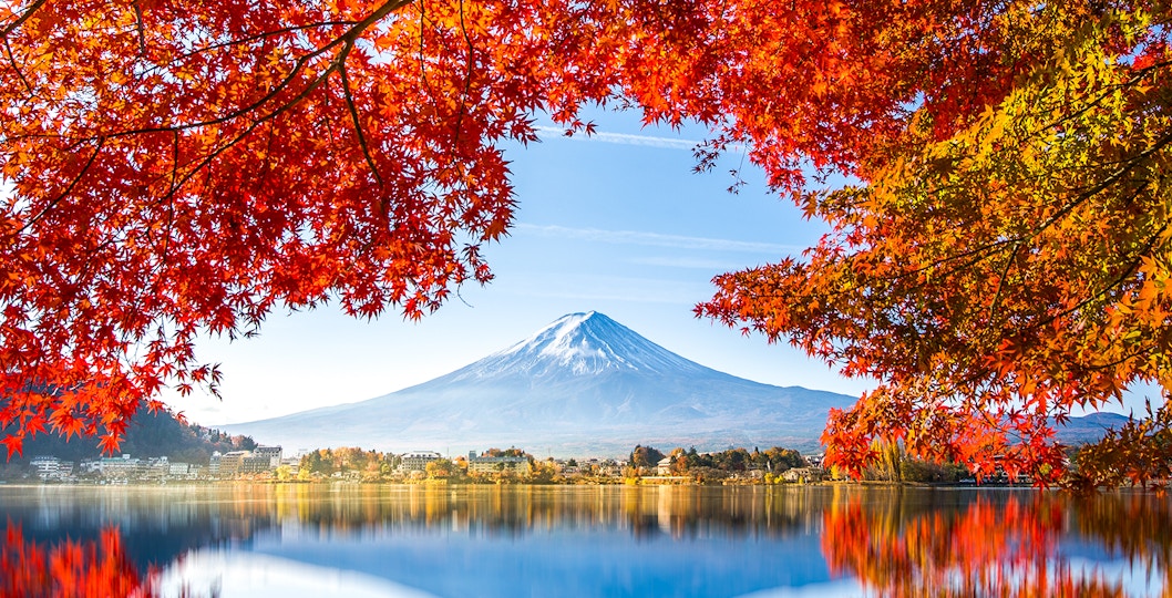 Reflection of Mt. Fuji in Lake Kawaguchi framed by autumn leaves.