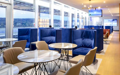 Primeclass Lounge seating area at Zurich Airport Terminal E with blue chairs and tables.