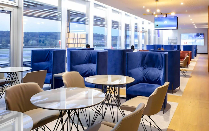 Primeclass Lounge seating area at Zurich Airport Terminal E with blue chairs and tables.