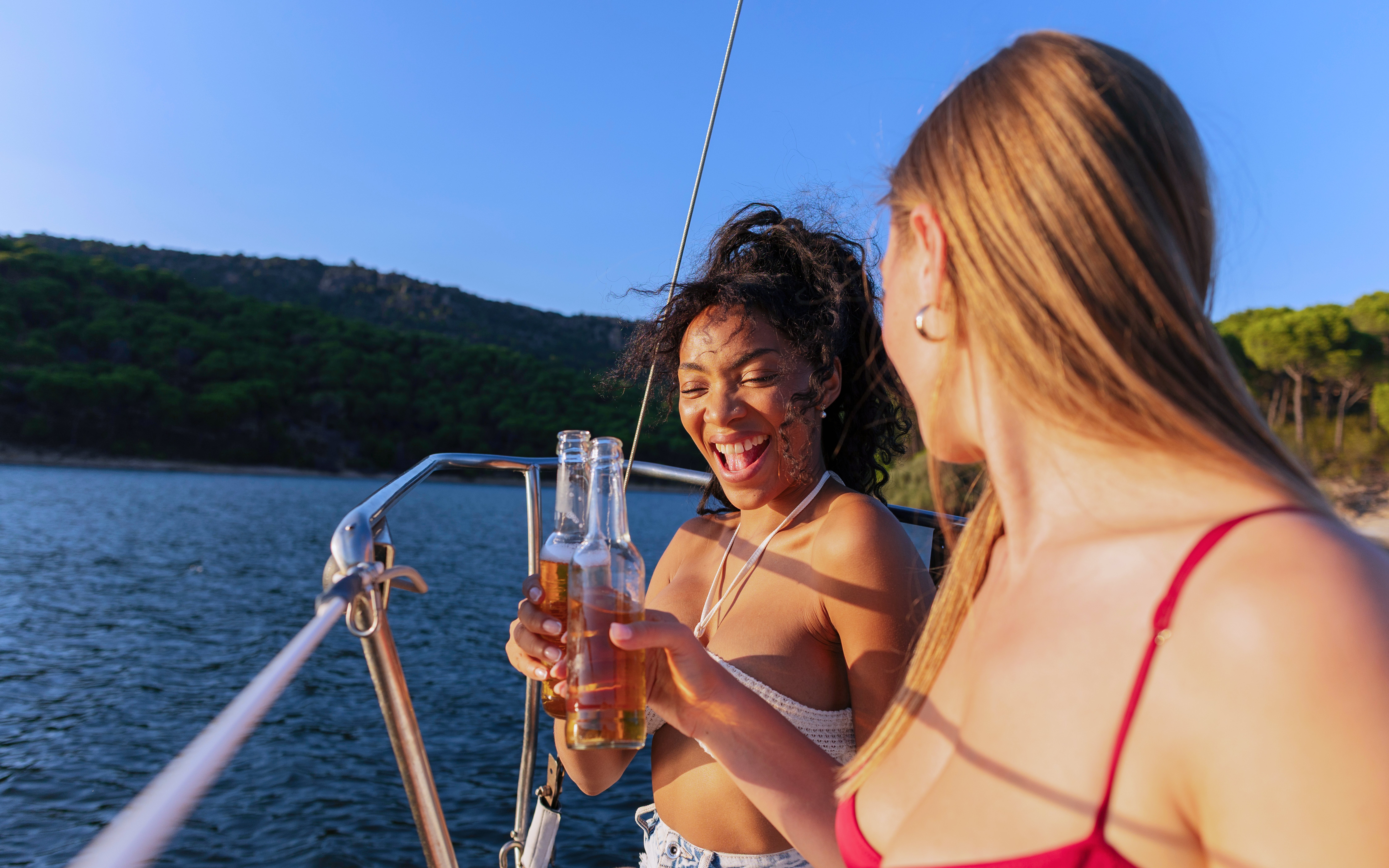 Friends toasting with drinks on a sailboat, enjoying a sunny day on the water.