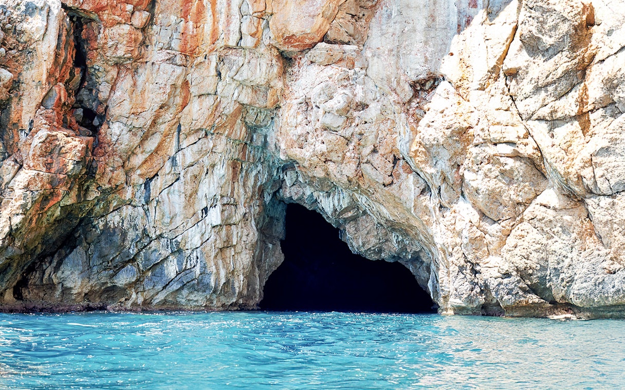Blue cave entrance in Kotor Bay with rocky cliffs and turquoise water.
