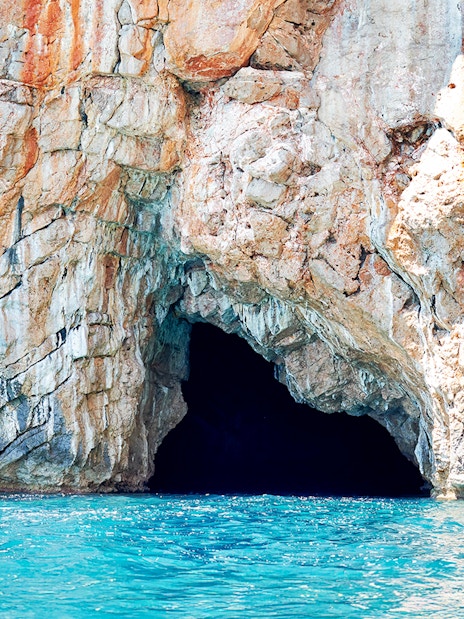 Blue cave entrance in Kotor Bay with rocky cliffs and turquoise water.