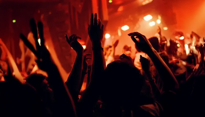 Concert crowd with raised hands in a dimly lit venue.