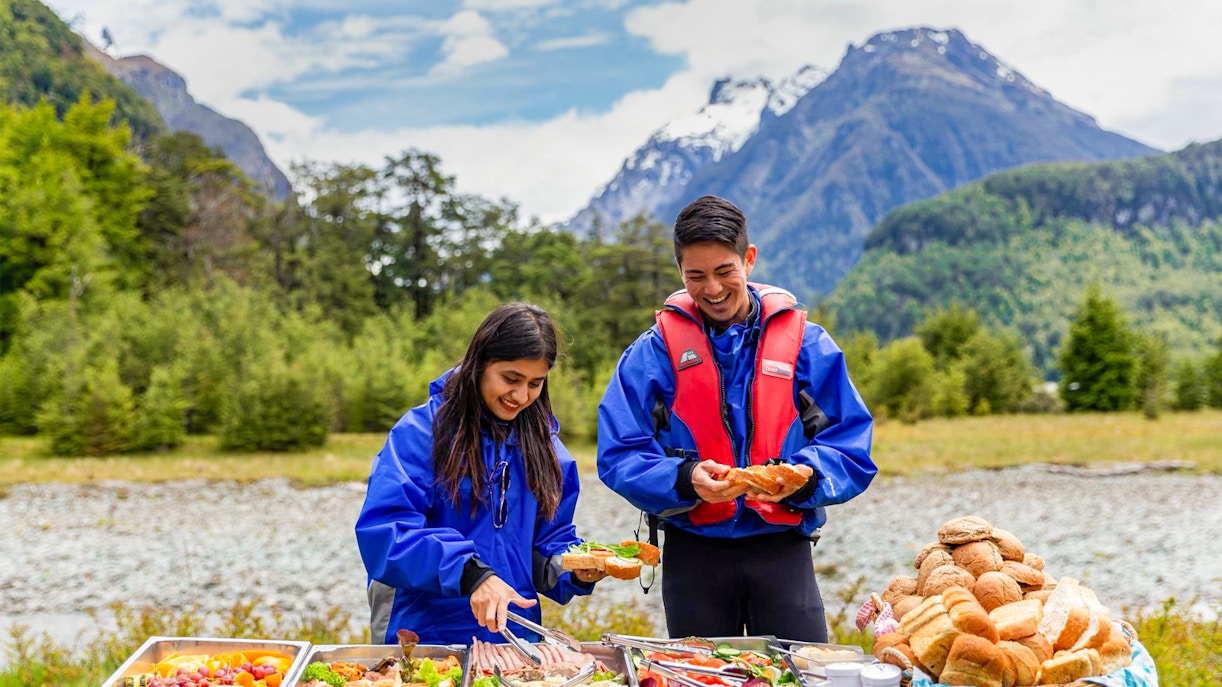 People enjoying a picnic with food trays in Dart River Funyaks, New Zealand.