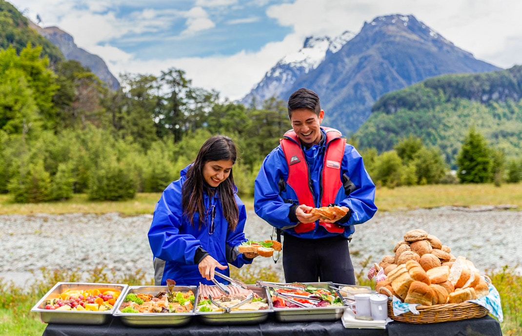 People enjoying a picnic with food trays in Dart River Funyaks, New Zealand.