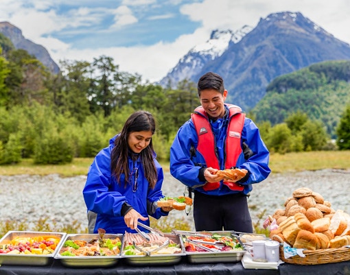 People enjoying a picnic with food trays in Dart River Funyaks, New Zealand.
